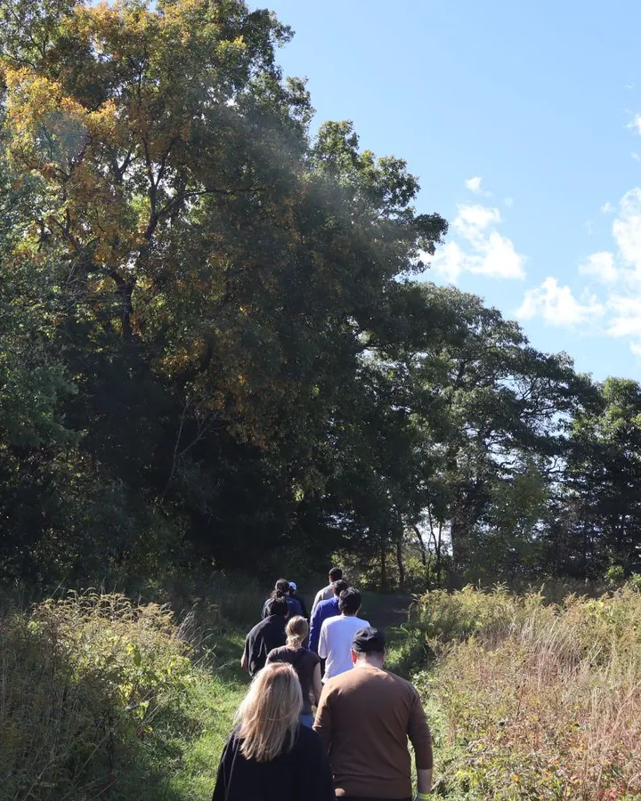 The team hiking single file along a grassy path under tall trees